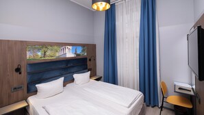A hotel room with a bed, a desk, a chair, a TV, and a window with curtains. - Smart Stay Hotel Station Munchen (Munich)