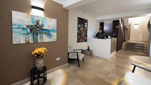 Eine Hotlelloge mit einer Rezeption, einem großen abstrakten Gemälde, einer Blumenvase und einer Treppe zu einer anderen Etage.