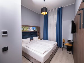 A modern hotel room with a large bed, a desk, a chair, a television, and a view of a building through a window. - Smart Stay Hotel Station Munchen (Munich)