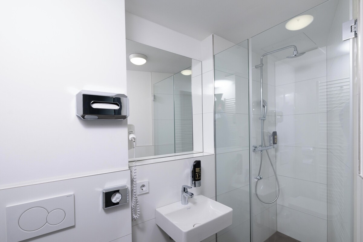 A modern bathroom with a glass shower enclosure, a white sink, and a built-in mirror.