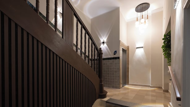 Eine moderne Treppe mit Holzgeländern und Handlauf, die zu einem Zwischenpodest mit einer Leuchte und einem Blumentopf führt.