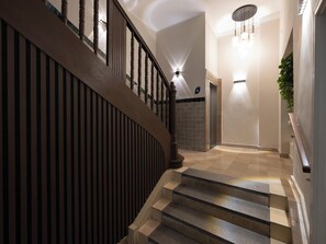 Una escalera moderna con barandillas y pasamanos de madera, que lleva a un rellano con una lámpara y una planta en maceta.