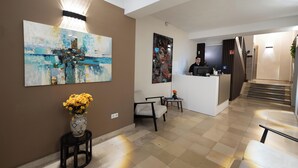 A hotel lobby with a reception desk, a large abstract painting, a vase with flowers, and a staircase leading to another floor. - Smart Stay Hotel Station Munchen (Munich)