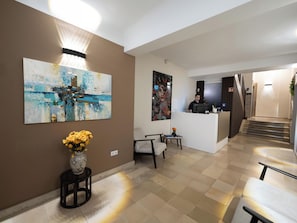 A hotel lobby with a reception desk, a large abstract painting, a vase with flowers, and a staircase leading to another floor. - Smart Stay Hotel Station Munchen (Munich)