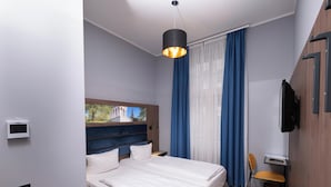 Ein modernes Hotelzimmer mit einem großen Bett, einem Schreibtisch, einem Sessel, einem Fernseher und Blick auf ein Gebäude durch ein Fenster.