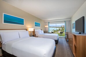 A hotel room with two beds, a TV, a desk, and a balcony with a view of the city.