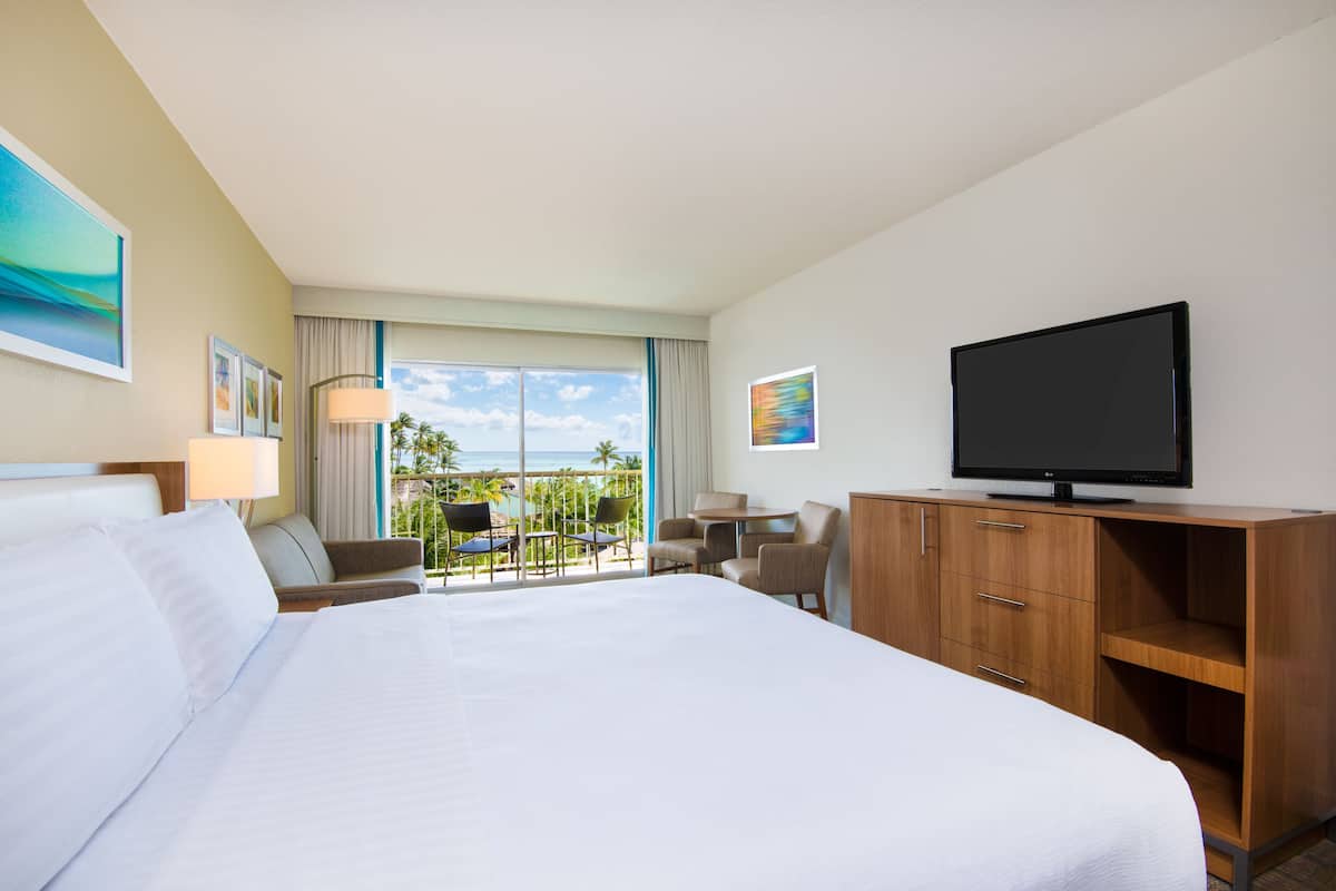 A hotel room with a large bed, a television, a desk, and a view of the ocean.