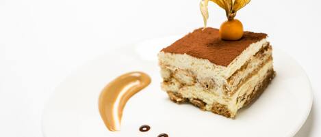 Una porción de postre en capas sobre un plato blanco, con una hoja decorativa y un hilo dorado.