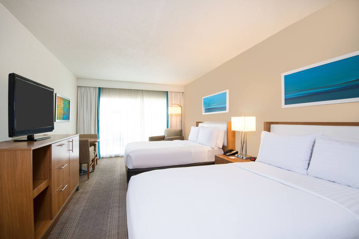 A hotel room with two beds, a TV, a desk, and a lamp.