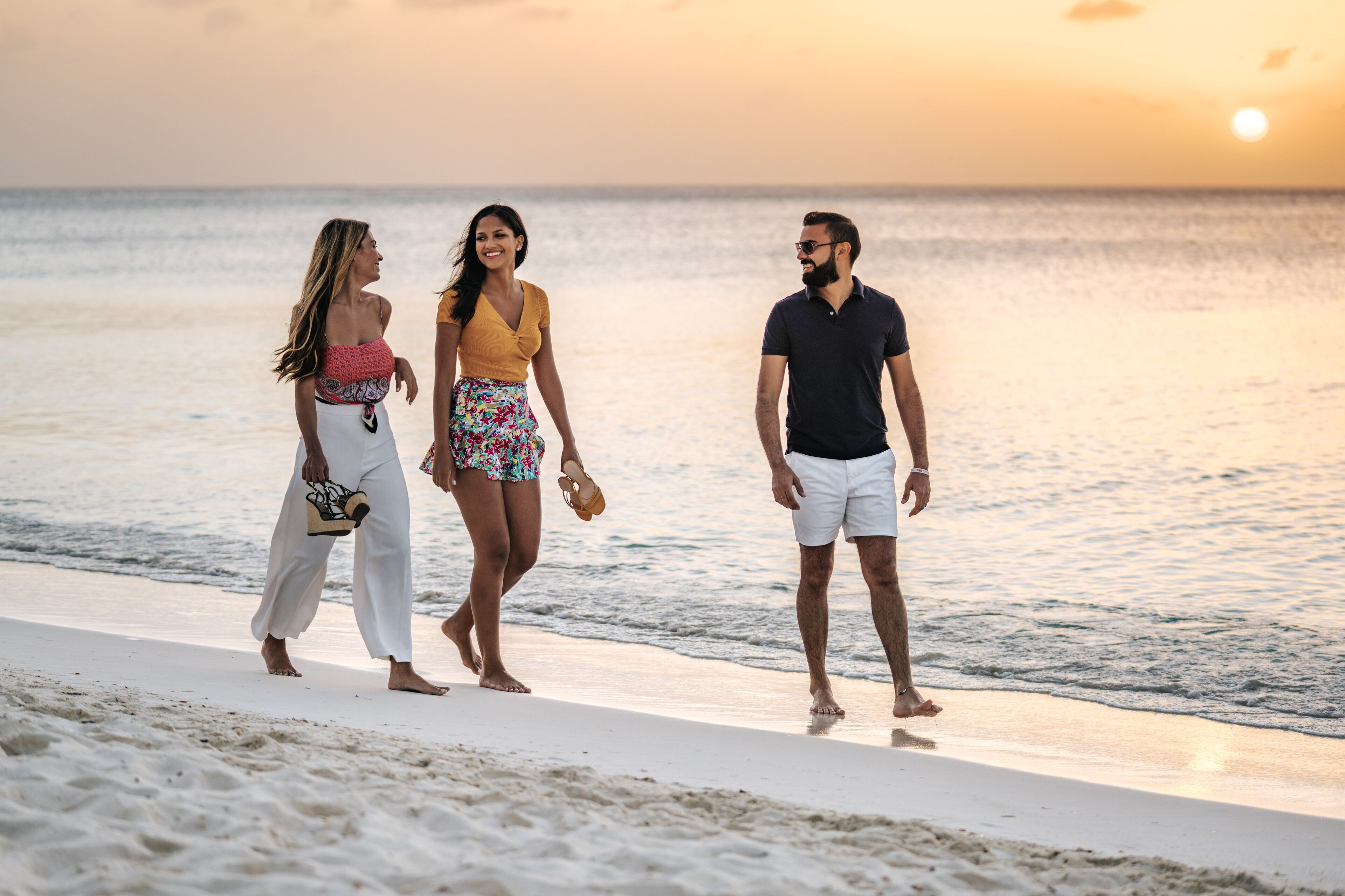 Tres personas caminando en una playa al atardecer.