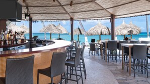 Un bar frente al mar con mostrador de baldosas, sillas de mimbre y sombrillas de paja.