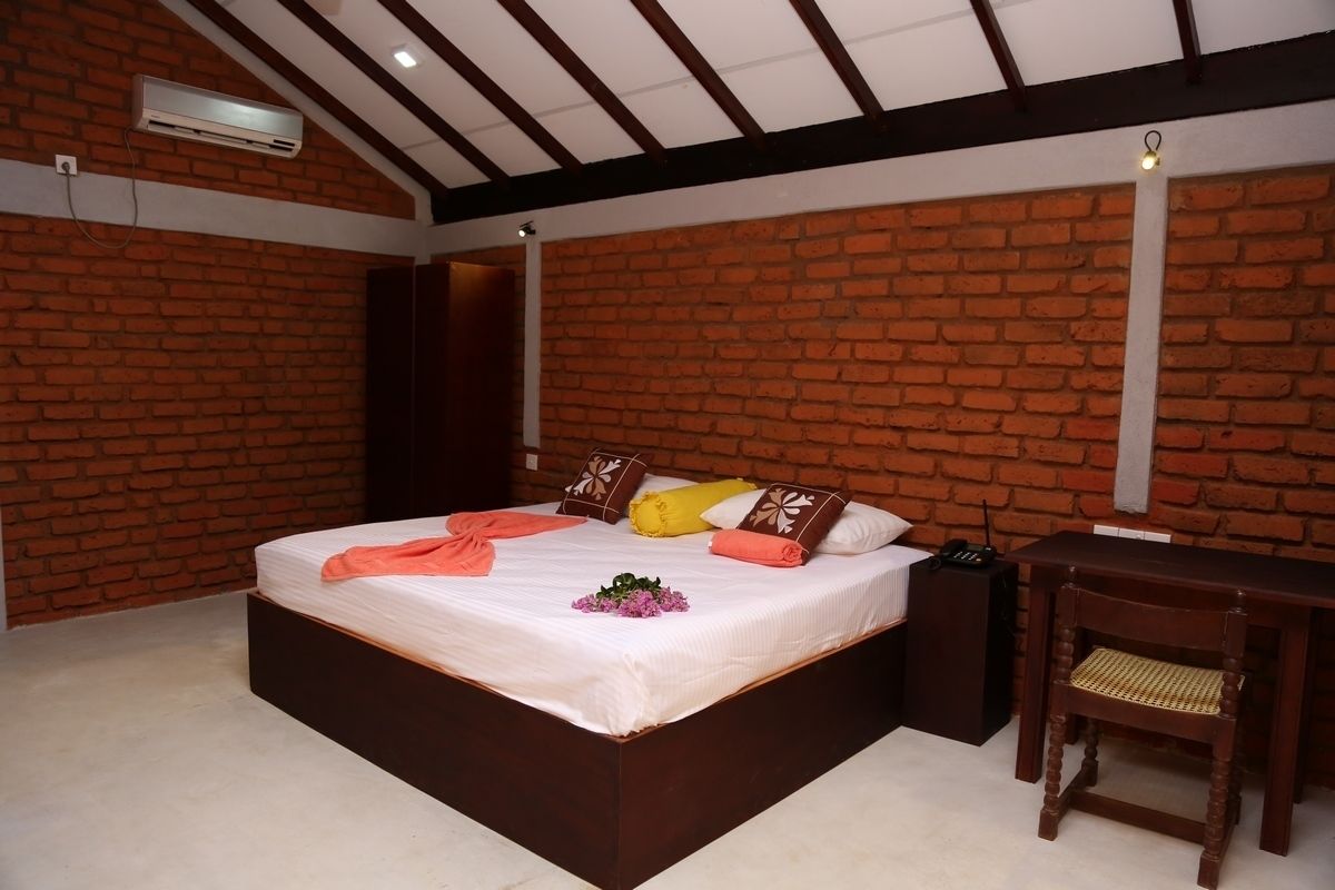 A bedroom with a brick wall, a bed with pillows, a bedside table, and an air conditioning unit.