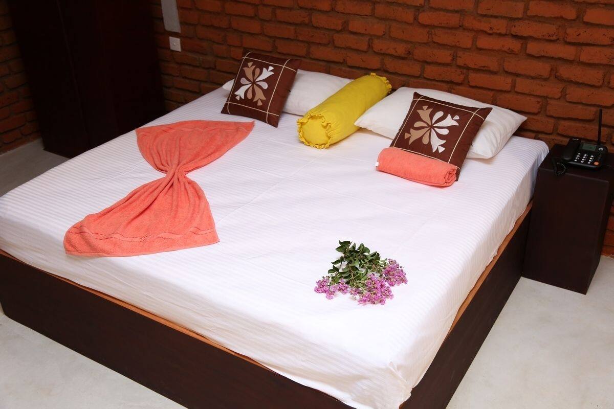 A neatly made bed with a white bedspread, a yellow rolled towel, and decorative pillows.