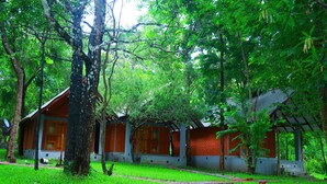 Un bâtiment traditionnel en bois, avec un toit rouge, entouré d’arbres et d’herbe verdoyants.