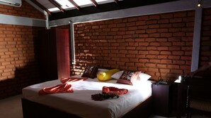 Une chambre avec un mur en briques, un lit recouvert de draps blancs et une table de chevet avec une lampe.