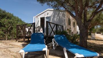 A small cabin with a porch and two blue lounge chairs.