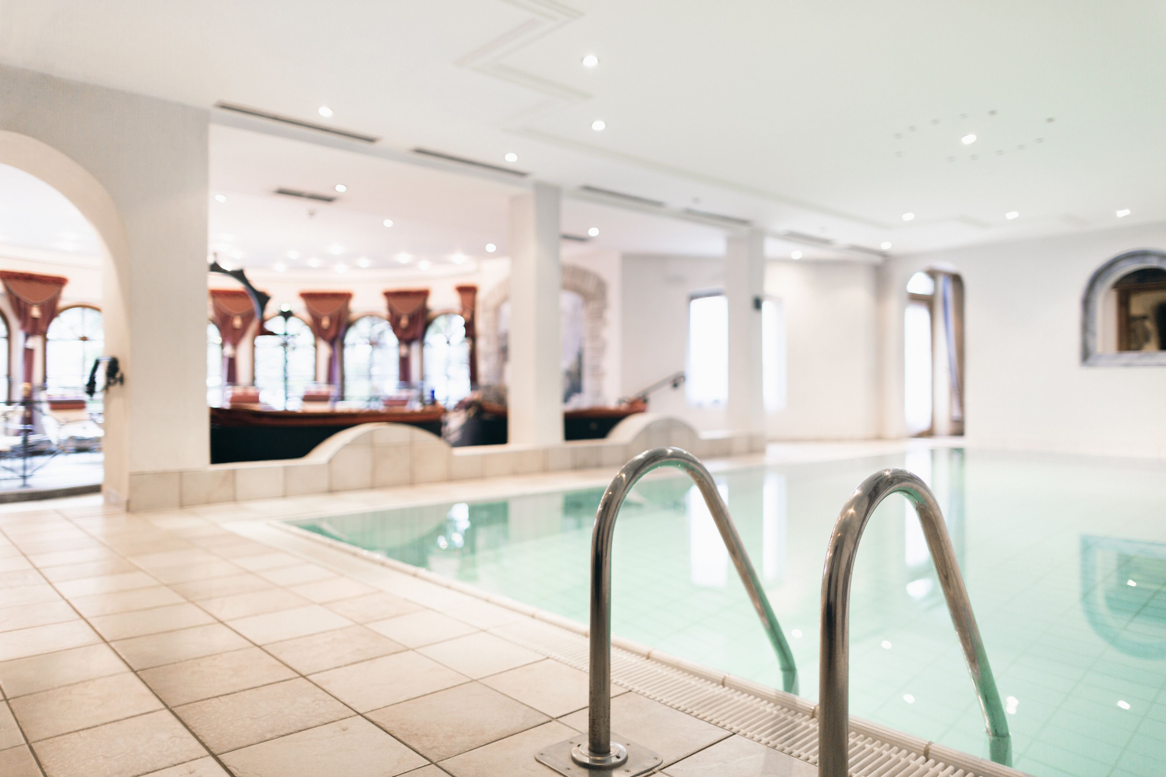 Una piscina con barandillas metálicas, suelo de baldosas y ventanas en arco al fondo.