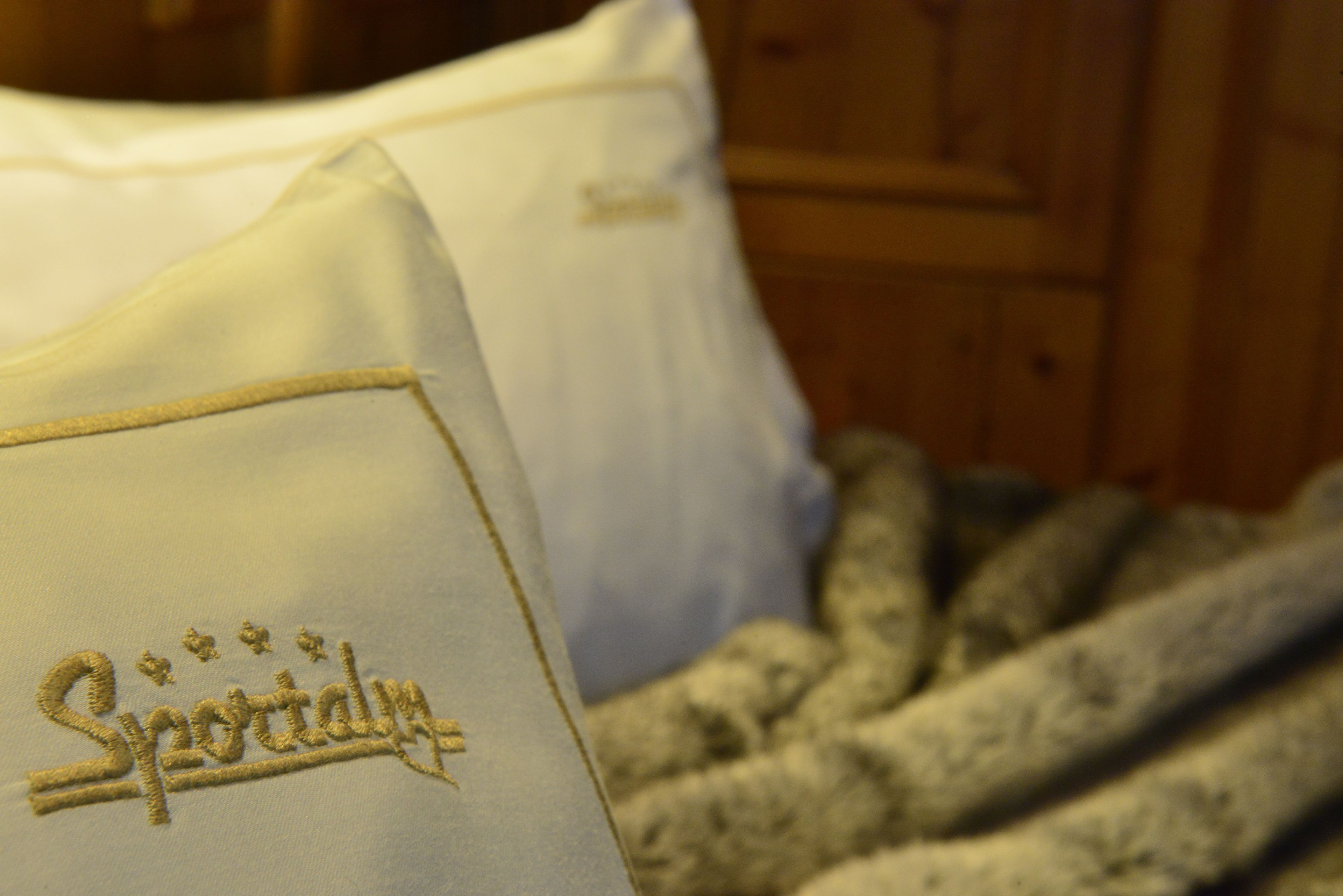 A bed with a white pillow featuring embroidered text.