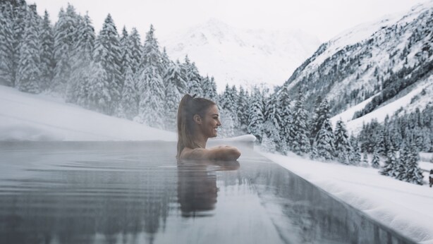 A person in a hot tub surrounded by snow-covered trees and mountains. - Alpine Resort Sportalm (Sankt Leonhard im Pitztal)