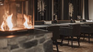 A cozy restaurant with a stone fireplace, dark curtains, and modern furniture. - Alpine Resort Sportalm (Sankt Leonhard im Pitztal)