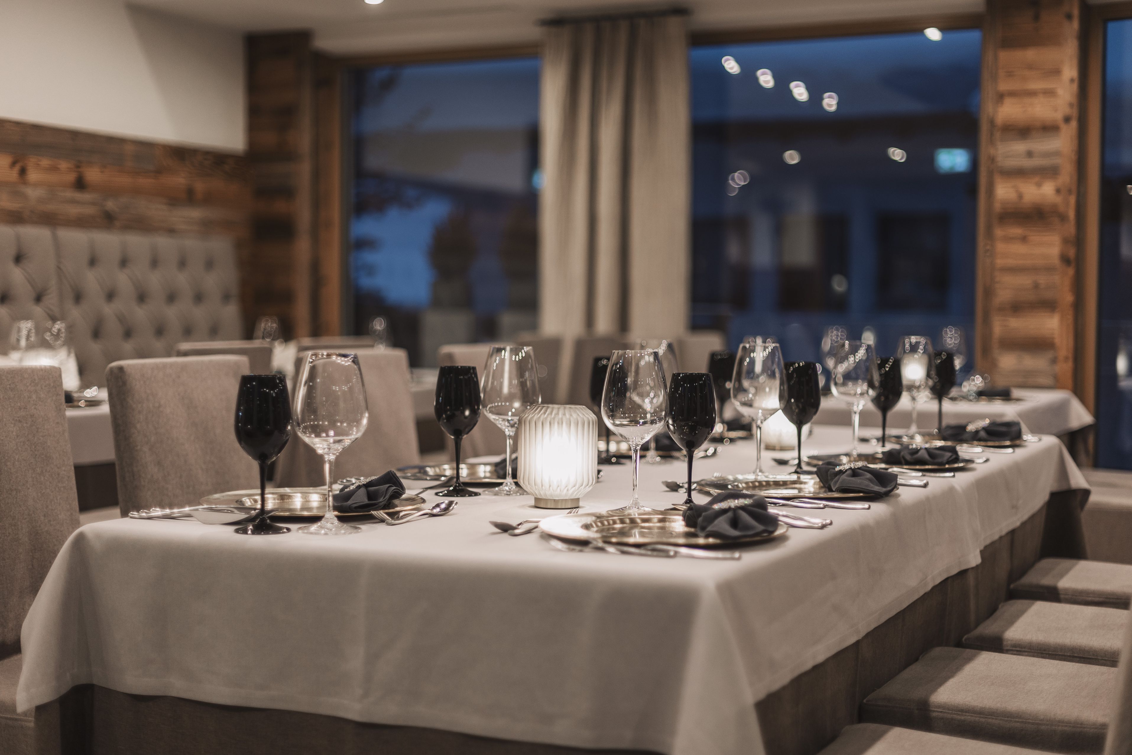 Un restaurante con una larga mesa dispuesta para una comida, con copas de vino, platos y cubiertos.