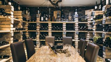 Una bodega con estantes y mesas de madera, llena de botellas y copas de vino.