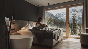 A modern bedroom with a large bed, a bedside table, a modern lamp, and a view of snow-capped mountains through a sliding glass door. - Alpine Resort Sportalm (Sankt Leonhard im Pitztal)