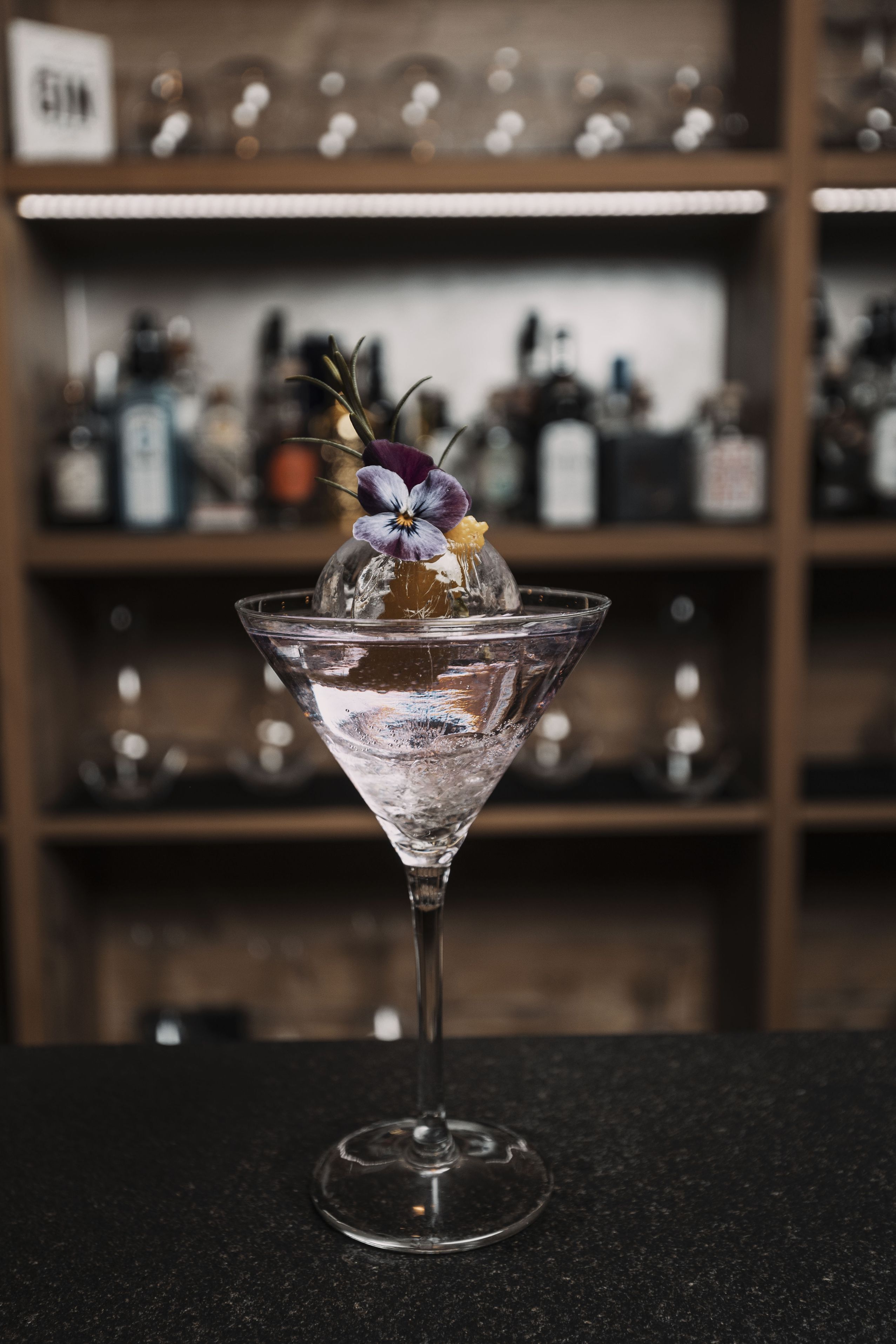 A martini glass with a flower garnish on a bar counter.