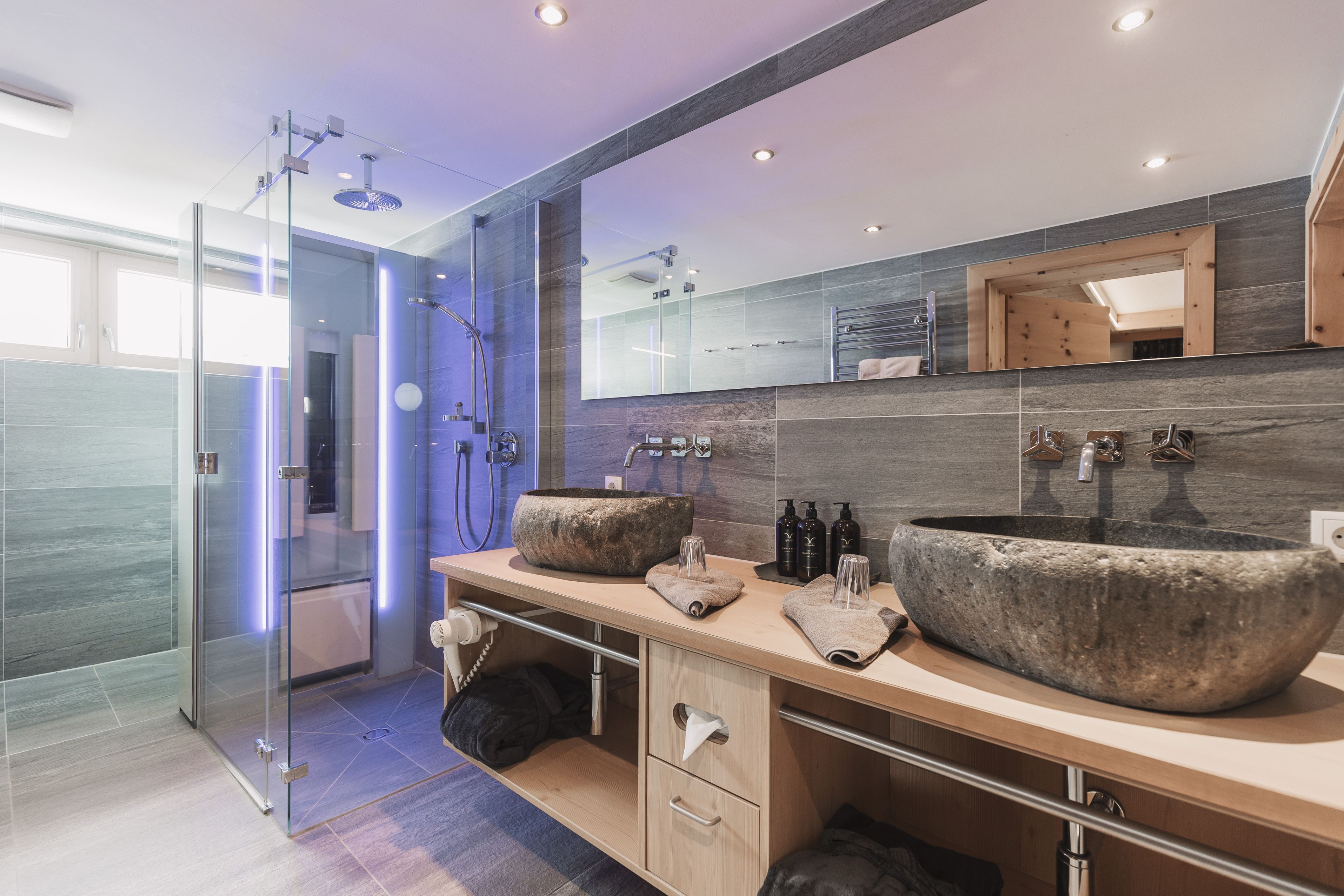 A modern bathroom with a glass-enclosed shower, two large stone sinks, and a large mirror.