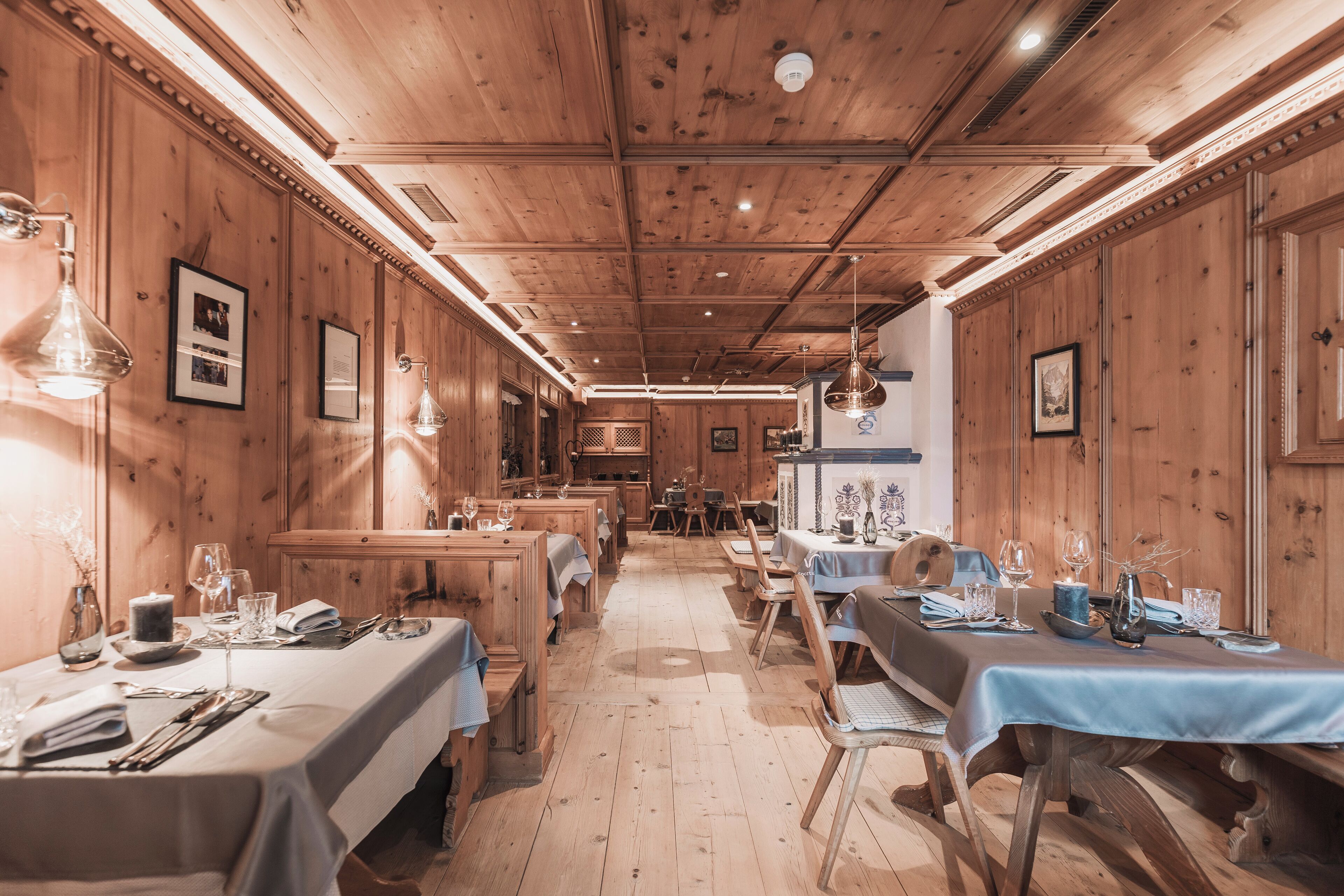 Un restaurant aux murs et au plafond en bois, avec des tables recouvertes de nappes blanches et agrémentées de serviettes bleues, et des tableaux encadrés qui décorent les murs.