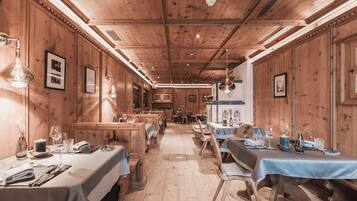 Un restaurant aux murs et au plafond en bois, avec des tables recouvertes de nappes blanches et agrémentées de serviettes bleues, et des tableaux encadrés qui décorent les murs.