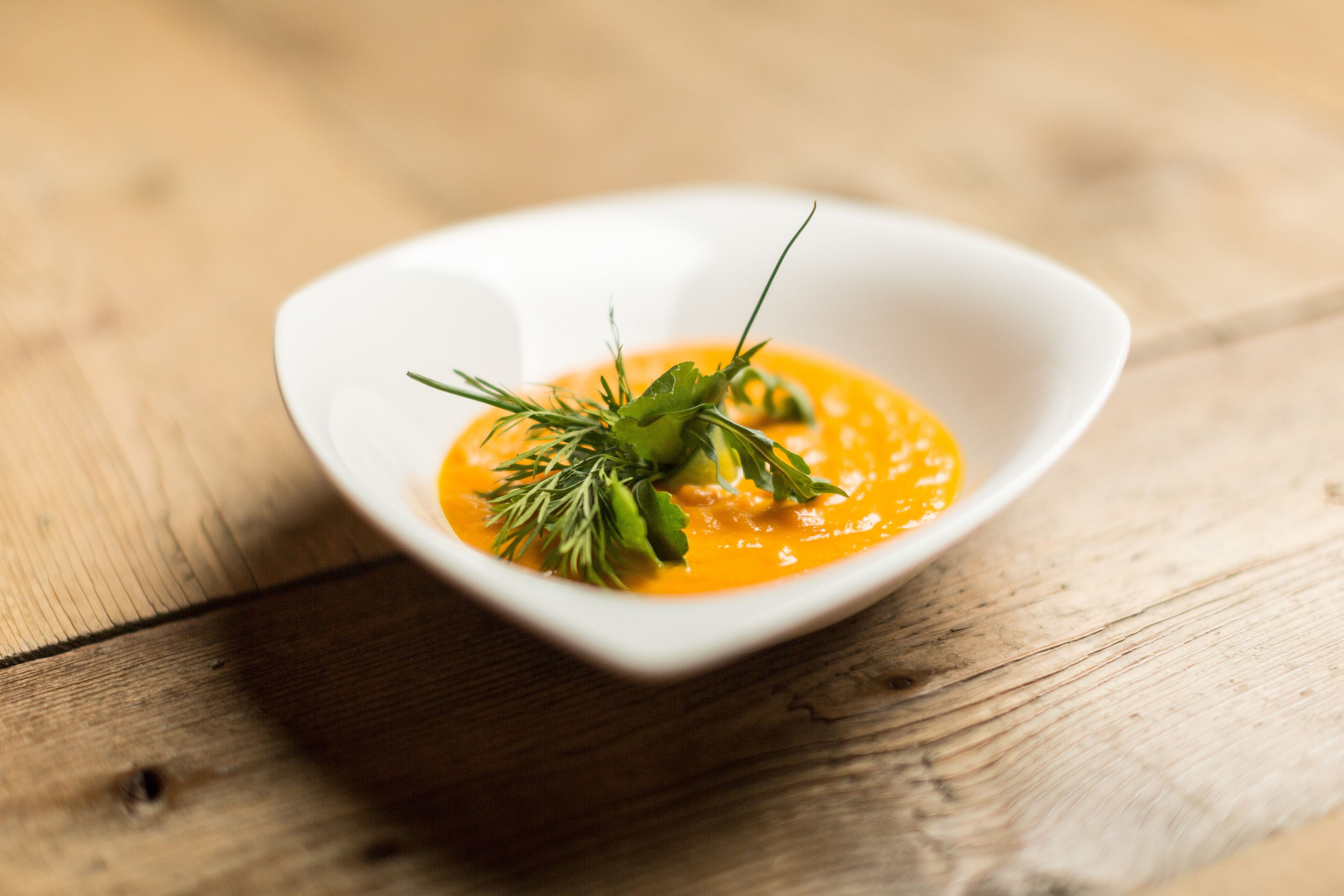 A white bowl of soup with a garnish on a wooden table.