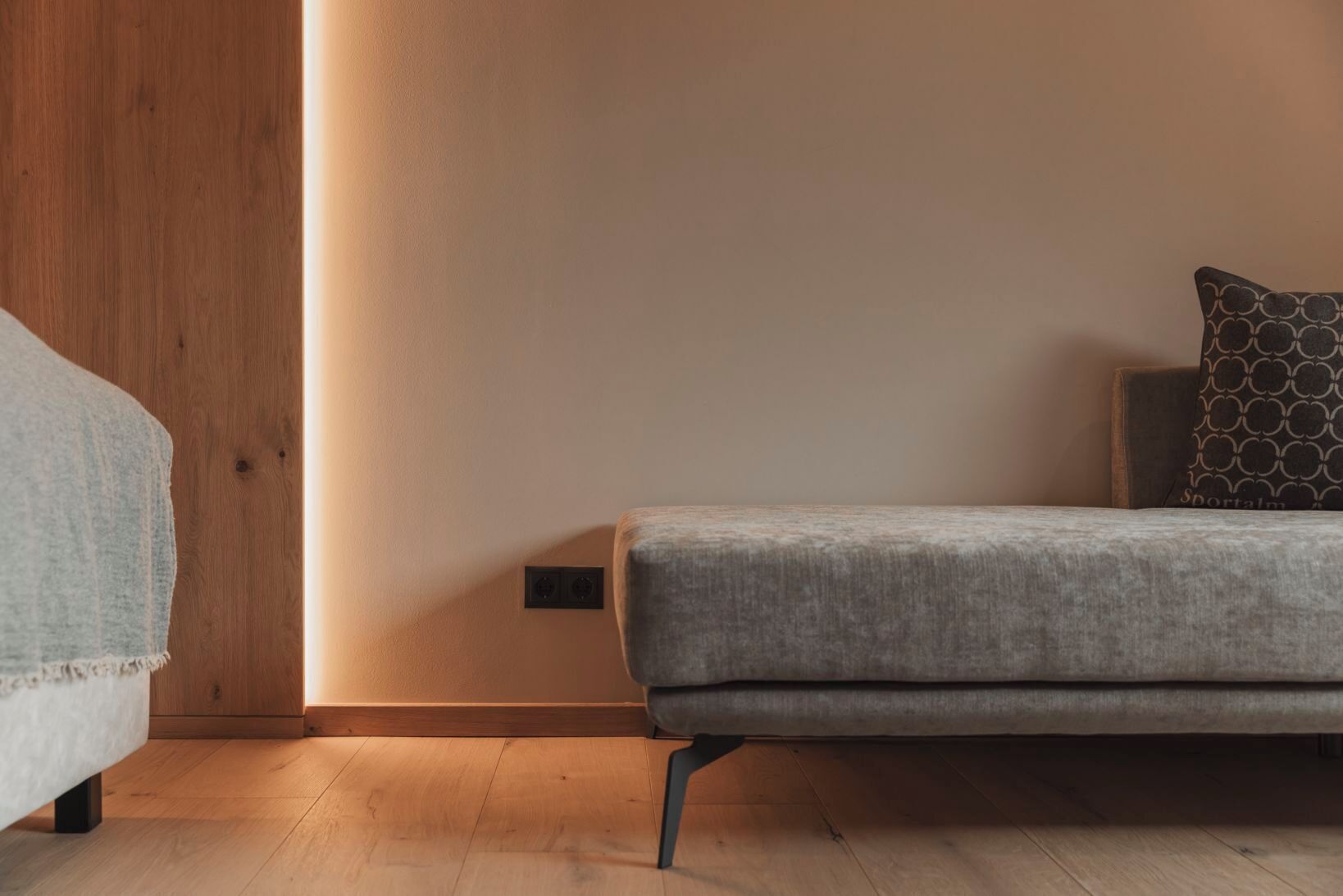 A minimalist room with a grey sofa, a patterned pillow, and a wooden wardrobe.