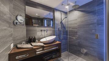Un baño moderno con un espejo grande, un tocador de madera, un lavabo sobre encimera y una zona de ducha con mampara de vidrio.