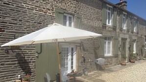 A stone building with a patio area featuring a table and chairs under a white umbrella. - Le Bois Gautier (Savigny-le-Vieux)