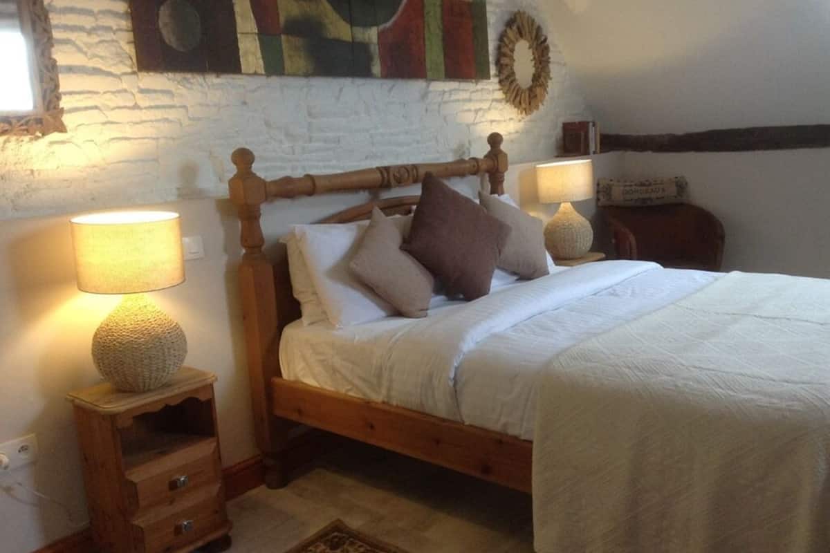 A cozy bedroom with a wooden bed, two bedside lamps, a small wooden nightstand, and a decorative wall piece.