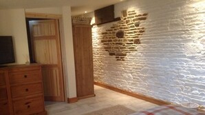 A bedroom with a stone wall, wooden dresser, and a plaid bedspread. - Le Bois Gautier (Savigny-le-Vieux)