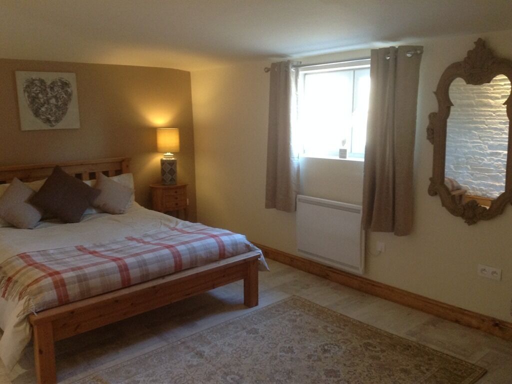 A bedroom with a wooden bed, a bedside lamp, a heart-shaped artwork, a window with curtains, and a mirror on the wall.