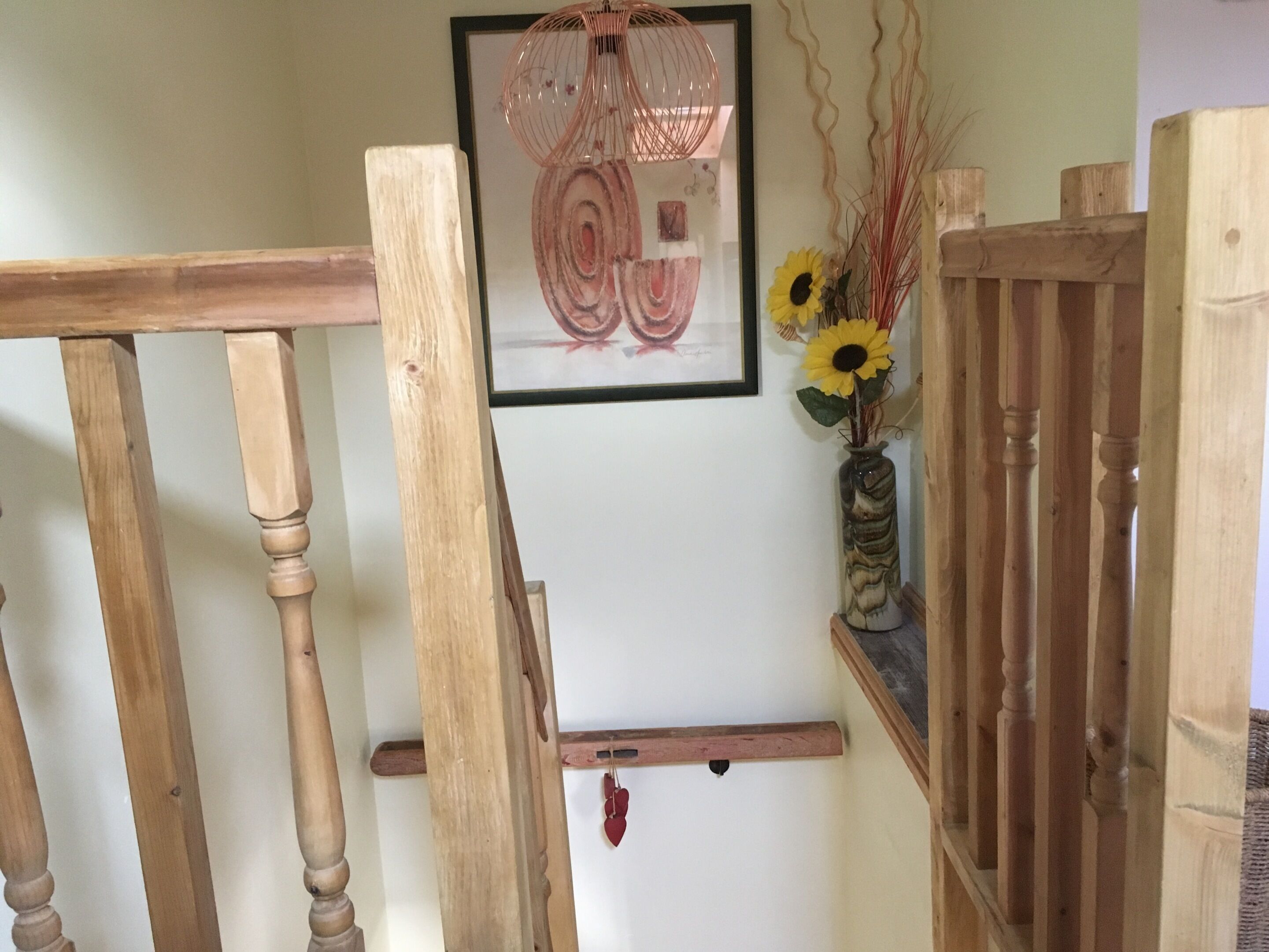 Una escalera de madera con barandilla, un cuadro enmarcado en la pared y un jarrón con girasoles.