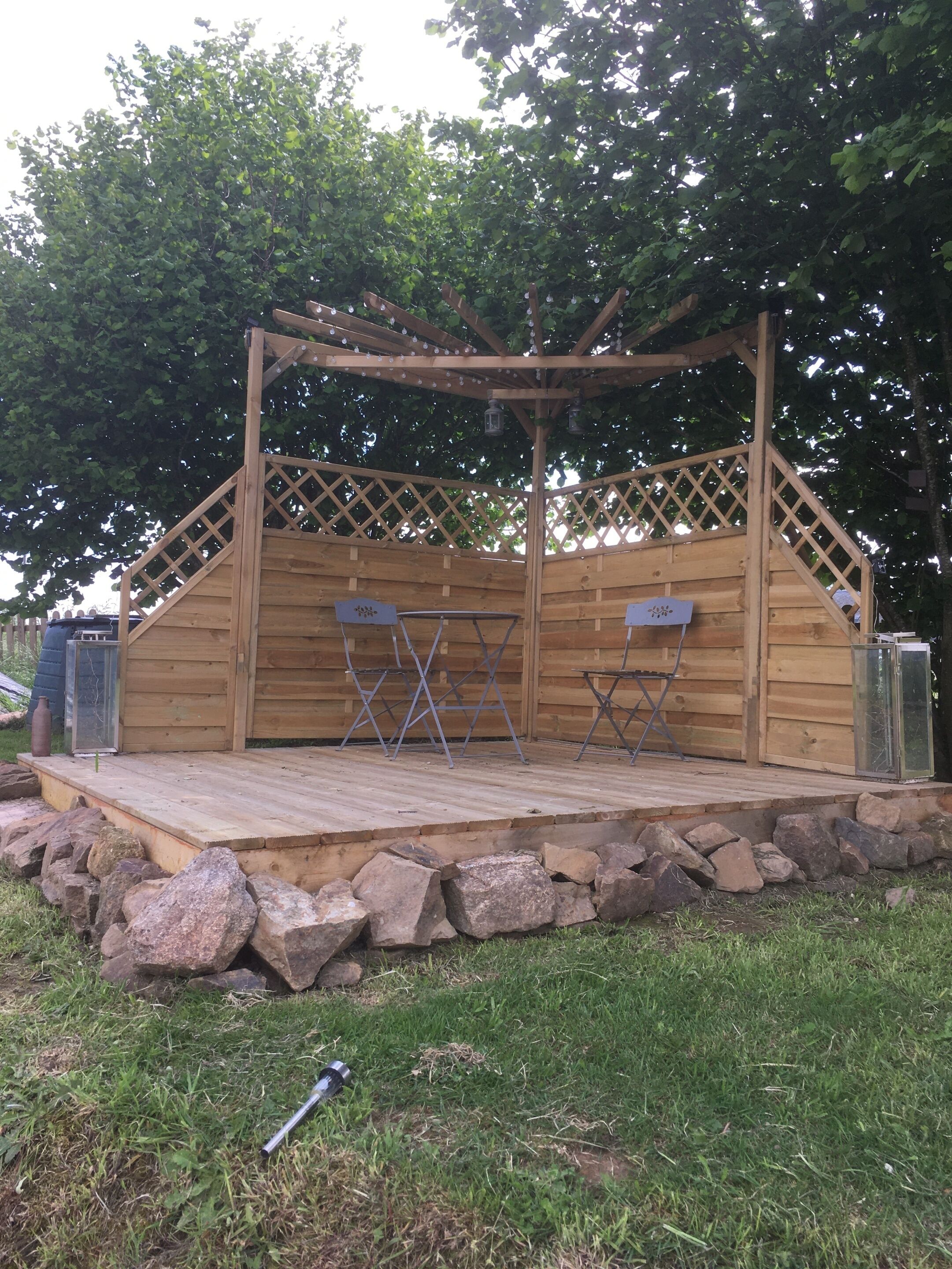 A wooden gazebo with a stage, seating, and lanterns.