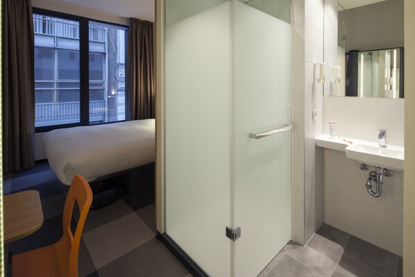 Una habitación de hotel con una cama, una silla, un ventanal que da al baño y una ventana con cortinas.