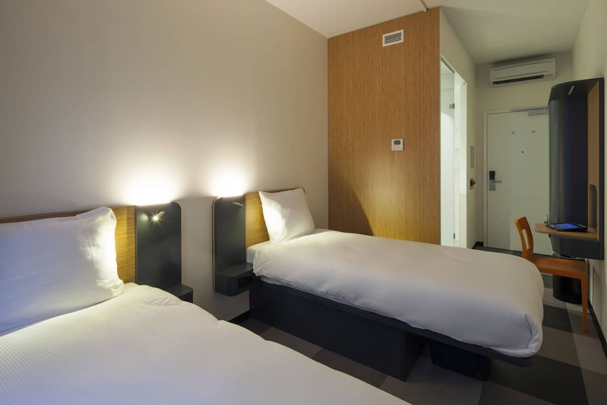 Ein Hotelzimmer mit zwei Einzelbetten, einer Wand im Holzoptik, einem Schreibtisch mit Stuhl und einer Klimaanlage.