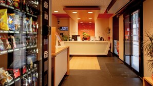 Ein Hotel-Empfangsbereich mit modernem Design, einem Empfangstresen, einem Fernseher und einem Getränkeautomaten.