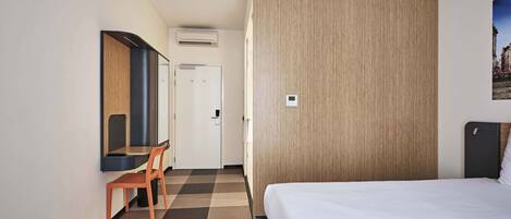 Una habitación de hotel con cama, escritorio con silla, armario y puerta.