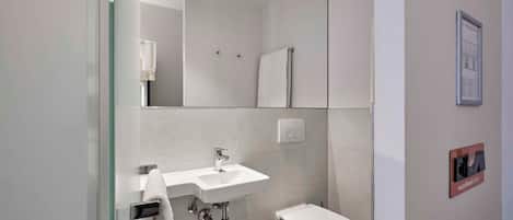 Un baño moderno con mampara de vidrio, un lavamanos blanco y un inodoro.