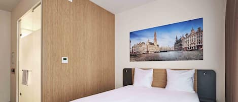 Una habitación de hotel con una cama, un panel de madera, un cuadro de paisaje urbano y una puerta.