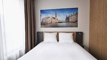 Een hotelkamer met een groot bed, een hoofdbord met houten afwerking en een lijst met een afbeelding van een historisch Europees stadsgezicht aan de muur.