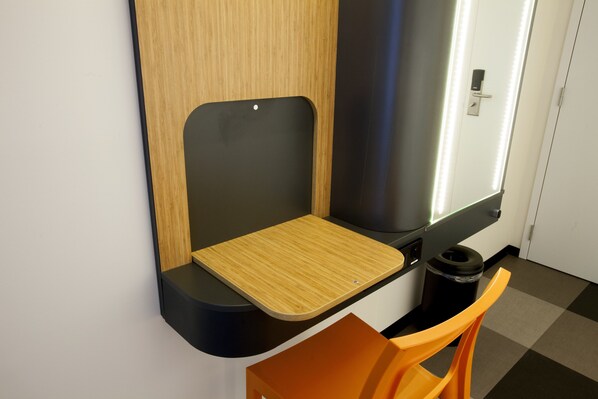 Un baño moderno con un tocador de madera, un cubo de basura negro y una silla naranja.