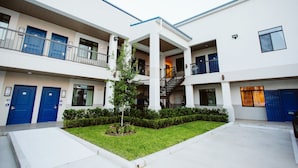 A multi-story building with blue doors, a central courtyard with a tree, and a staircase connecting the floors.