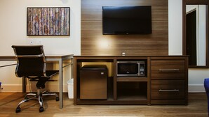 A hotel room with a desk, chair, flat-screen TV, microwave, and a small refrigerator.